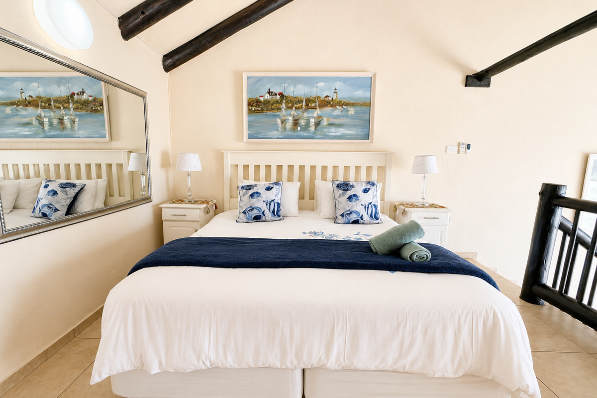 A cozy bedroom featuring exposed timber ceiling beams, tiled flooring, and a timber balustrade overlooking the lower level.