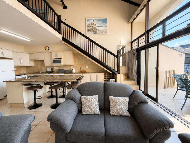 Spacious open-plan living and kitchen area featuring a mezzanine level, granite countertops, and large sliding doors leading to an outdoor patio.