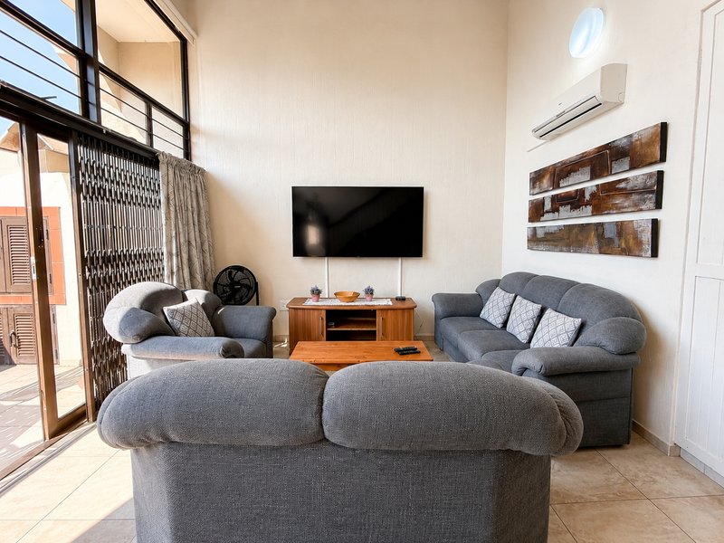 A bright living room featuring high ceilings, tiled flooring, and large sliding glass doors that provide ample natural light and access to the balcony.