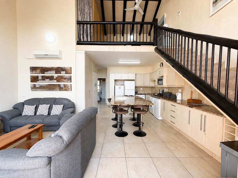 Spacious open-plan living and kitchen area featuring granite countertops, built-in cabinetry, a mezzanine level, and exposed timber ceiling beams.