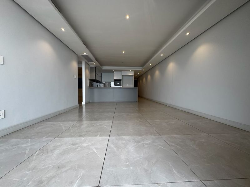 A spacious, modern open-plan living and kitchen area featuring large-format porcelain floor tiles, recessed ceiling lighting, and sleek built-in cabinetry.