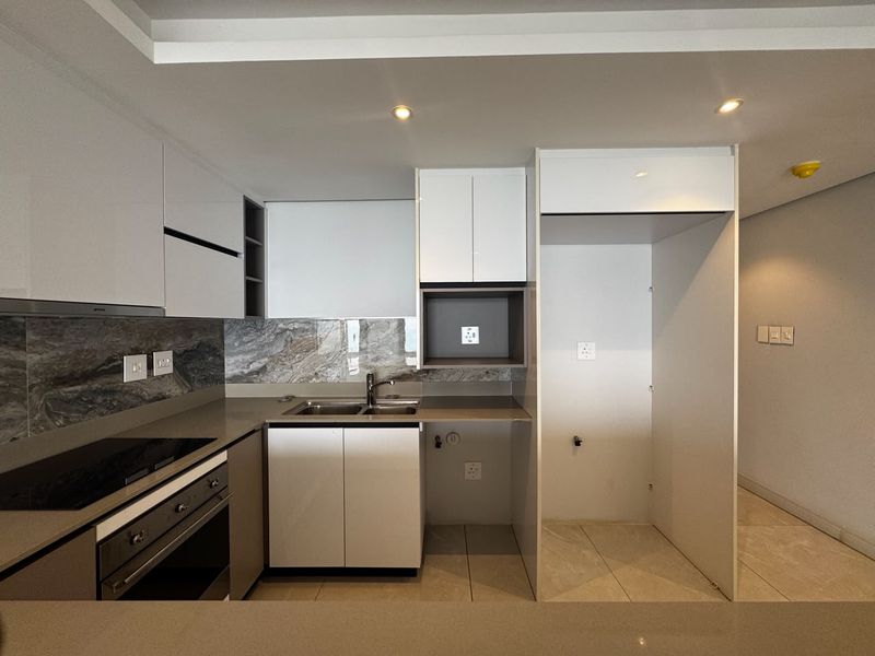 Modern kitchen featuring sleek white cabinetry, stone countertops, integrated oven and hob, and a stylish stone splashback in a clean, contemporary apartment setting.