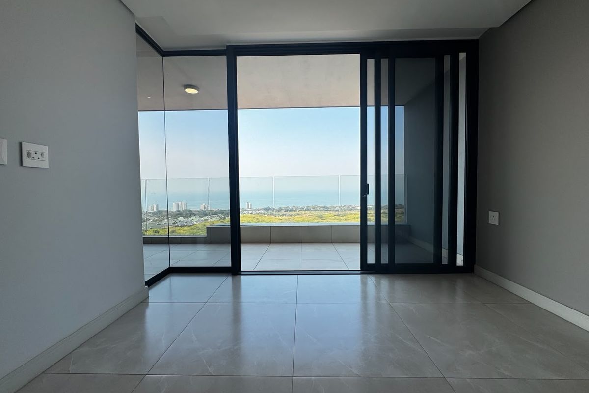 Modern, empty living area featuring large format floor tiles and expansive sliding glass doors opening onto a balcony with panoramic coastal views.