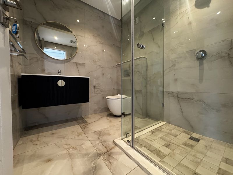 Modern bathroom featuring a wall-mounted vanity, wall-hung toilet, and a spacious glass-enclosed shower with high-quality marble-look tiling throughout.