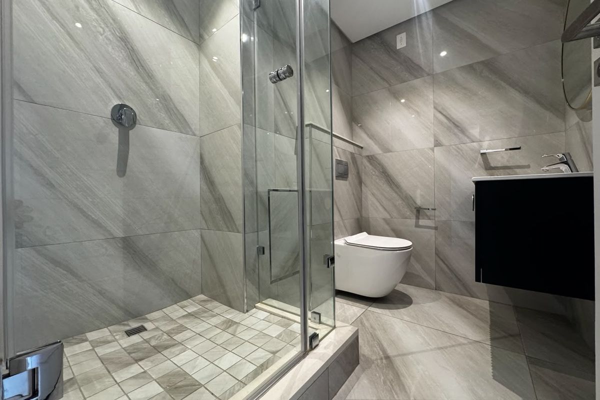 Modern bathroom featuring a walk-in glass shower, wall-mounted toilet, and sleek vanity cabinet with contemporary grey tiled finishes.