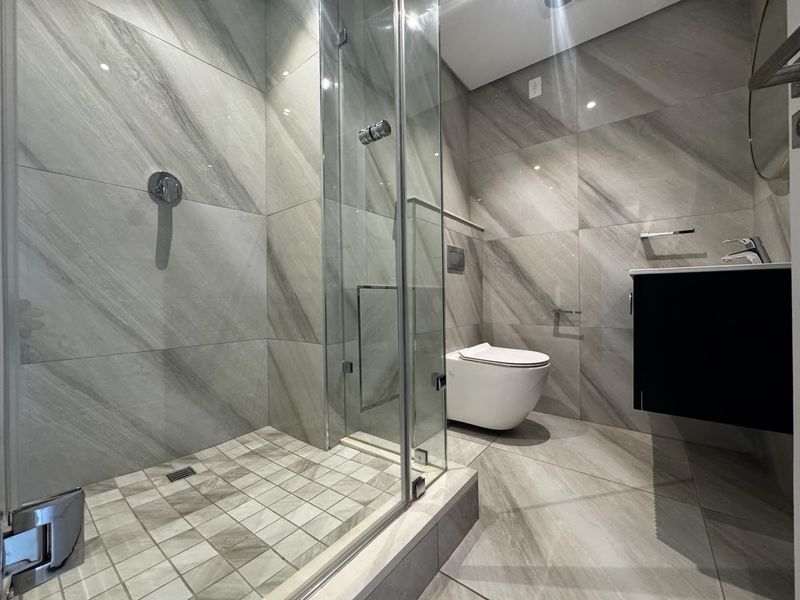 Modern bathroom featuring a walk-in glass shower, wall-mounted toilet, and sleek vanity cabinet with contemporary grey tiled finishes.