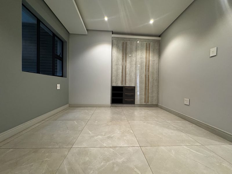 A modern, empty bedroom featuring high-quality tiled flooring, recessed ceiling lighting, and sleek built-in cupboards with contemporary finishes.