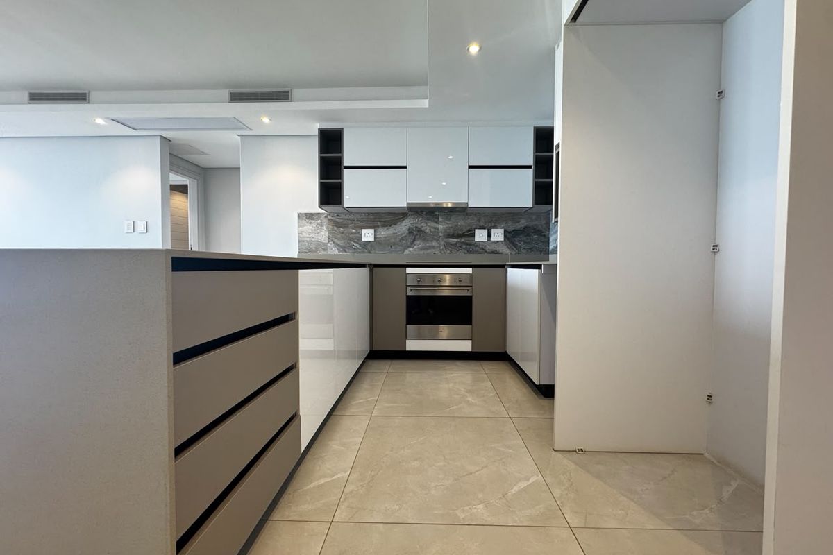 Modern kitchen featuring sleek white and grey cabinetry, stone countertops, integrated oven, extractor fan, and large format stone floor tiles.