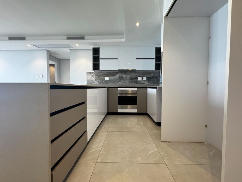 Modern kitchen featuring sleek white and grey cabinetry, stone countertops, integrated oven, extractor fan, and large format stone floor tiles.