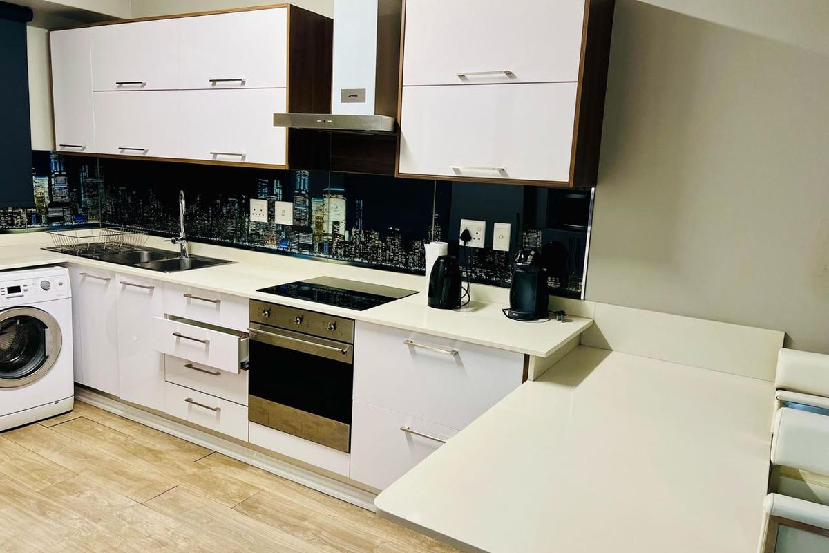Modern kitchen featuring white cabinetry, stone countertops, integrated appliances, and a unique city-scape splashback, offering a clean and functional cooking space.