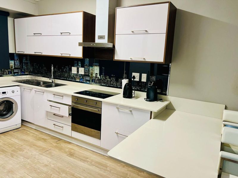 Modern kitchen featuring white cabinetry, stone countertops, integrated appliances, and a unique city-scape splashback, offering a clean and functional cooking space.