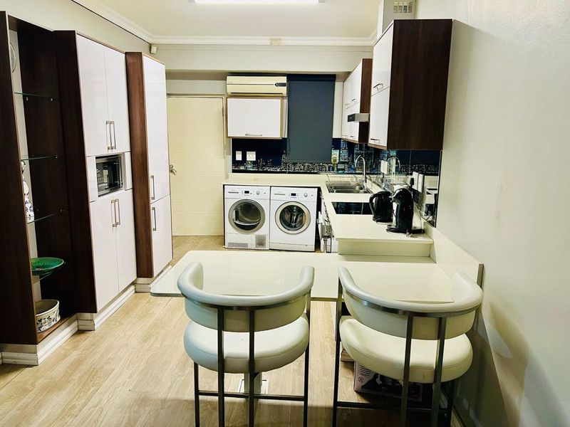 A functional kitchen featuring modern built-in cabinetry, integrated appliances, a breakfast counter, and laminate flooring, providing a compact and efficient workspace.