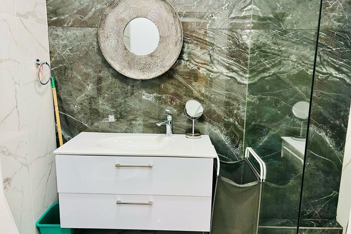 Modern bathroom featuring a white vanity cabinet with integrated basin, mixer tap, and striking dark marble-effect wall tiling with a glass shower screen.