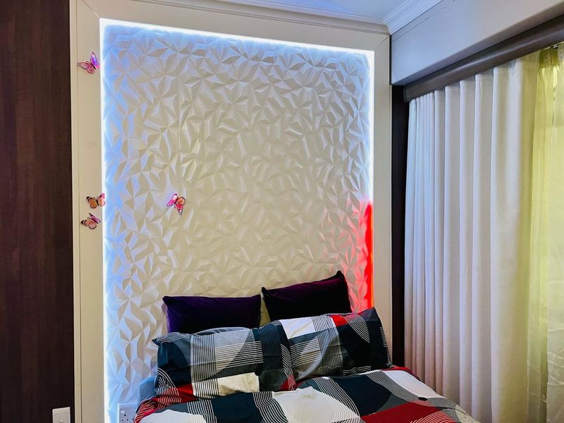 A bedroom featuring a modern textured 3D accent wall with integrated LED backlighting and ceiling coving.