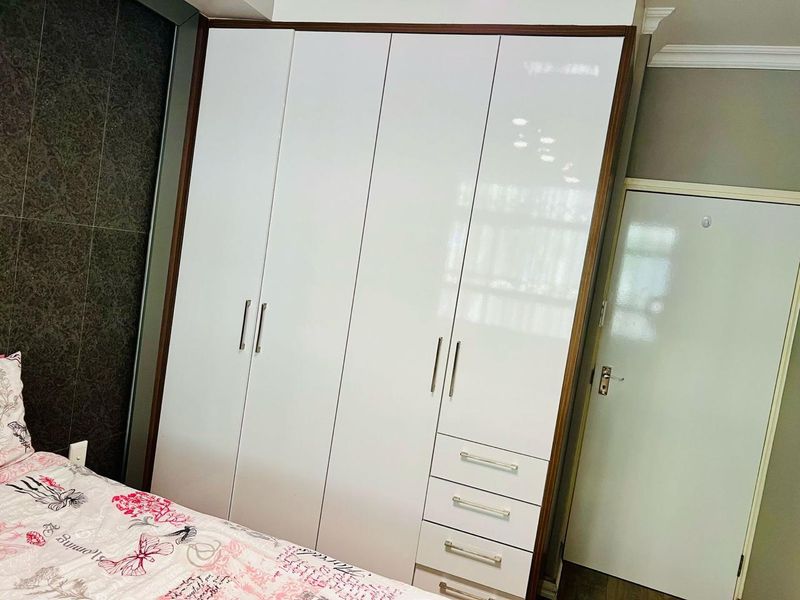 A bedroom featuring a modern, high-gloss white built-in wardrobe with integrated drawers and dark wood trim detailing.