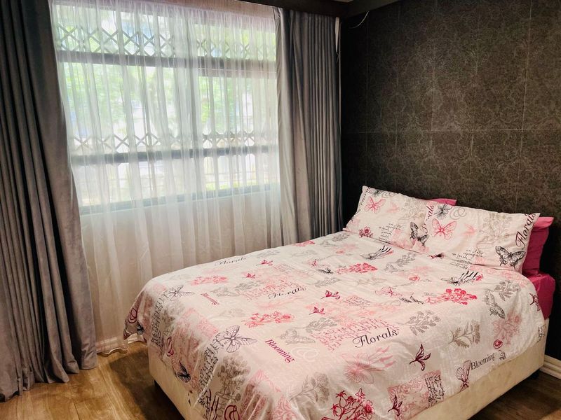 A cozy bedroom featuring laminate flooring, a textured feature wall, and a window fitted with a security gate and curtains.