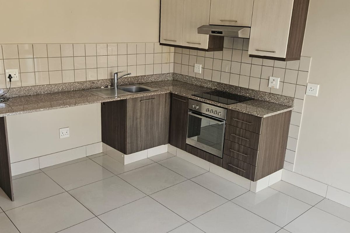 A clean, modern kitchen featuring granite countertops, built-in oven, electric hob, extractor fan, and ample cabinetry, finished with neutral tiled flooring and backsplash.