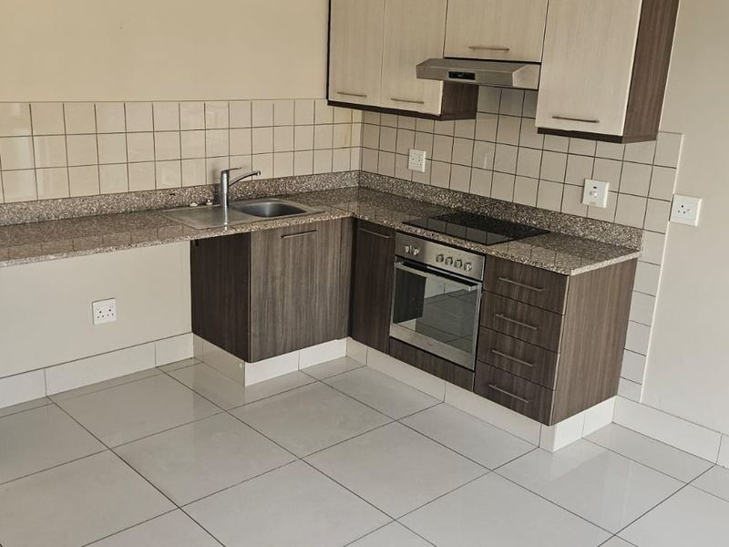 A clean, modern kitchen featuring granite countertops, built-in oven, electric hob, extractor fan, and ample cabinetry, finished with neutral tiled flooring and backsplash.