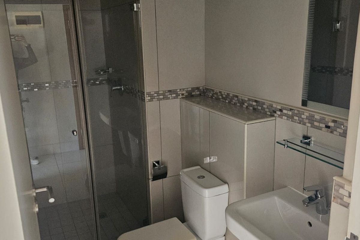 A clean, functional bathroom featuring a glass shower enclosure, wall-mounted toilet, and vanity basin with neutral tiling and mosaic accents.