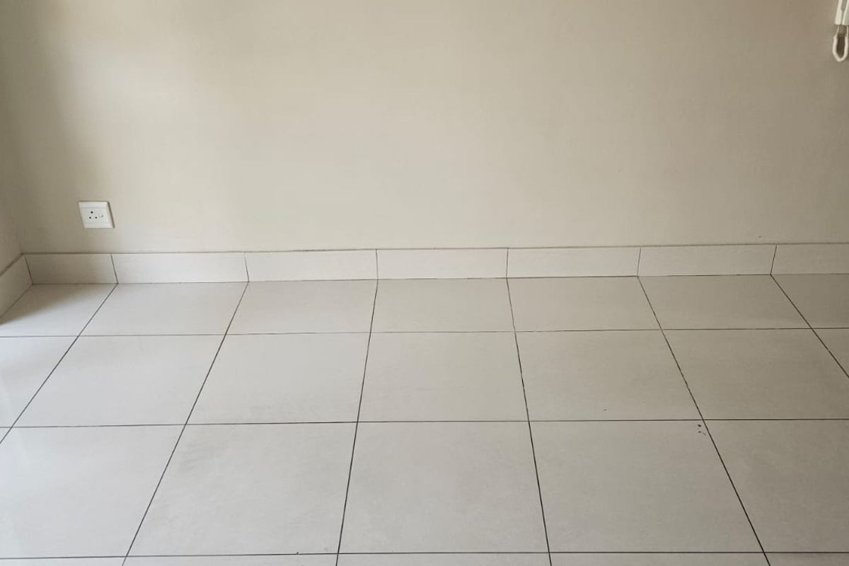 An empty living area featuring neutral tiled flooring, matching tiled skirting, and a sliding glass door providing natural light.