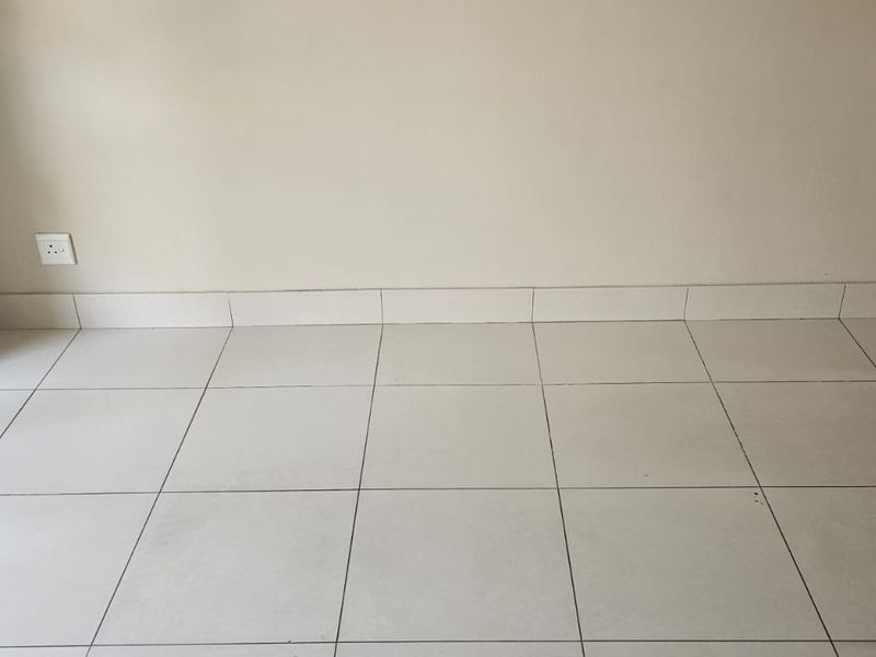 An empty living area featuring neutral tiled flooring, matching tiled skirting, and a sliding glass door providing natural light.