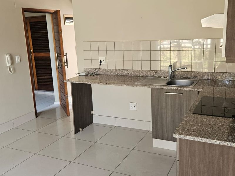 A functional kitchen featuring granite countertops, built-in cabinetry, a ceramic tile backsplash, and an integrated electric hob, presented in a clean, empty space.