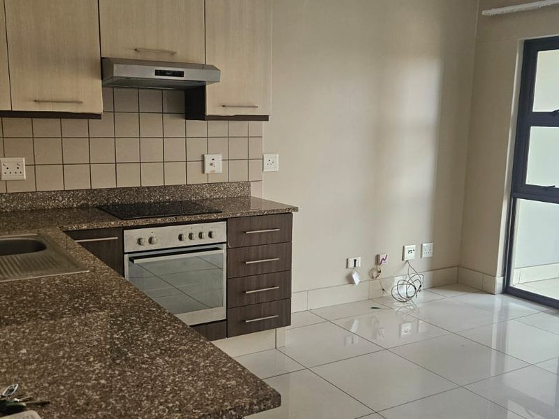 Modern open-plan kitchen featuring stone countertops, built-in oven and hob, and tiled flooring, with direct access to a balcony through a sliding glass door.