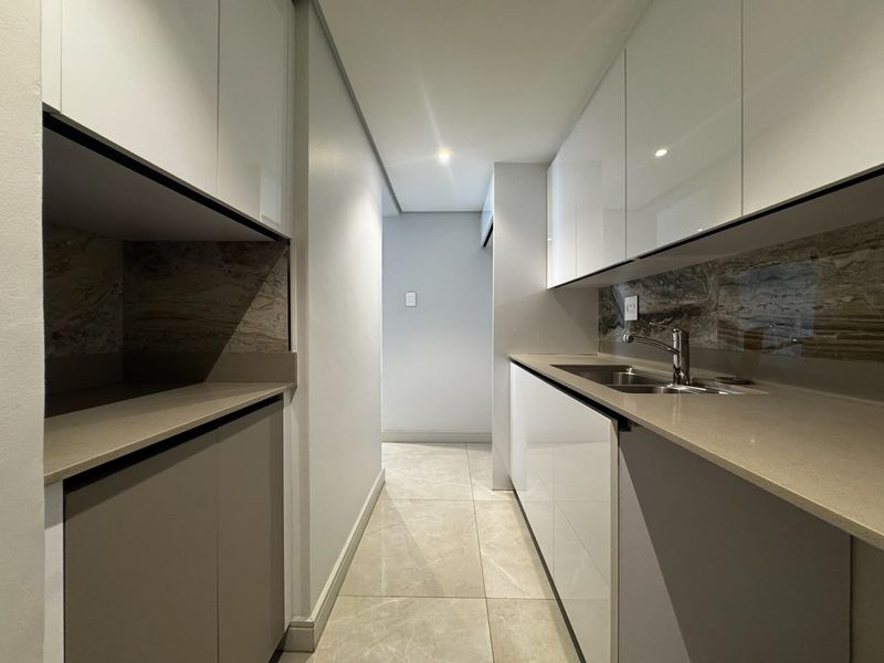 A modern, minimalist scullery featuring sleek high-gloss cabinetry, stone countertops, and a contemporary undermount sink with a stone splashback.