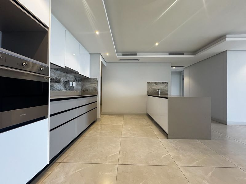 Modern, minimalist kitchen featuring sleek cabinetry, stone countertops, a central island, built-in appliances, and high-quality tiled flooring in an open-plan layout.