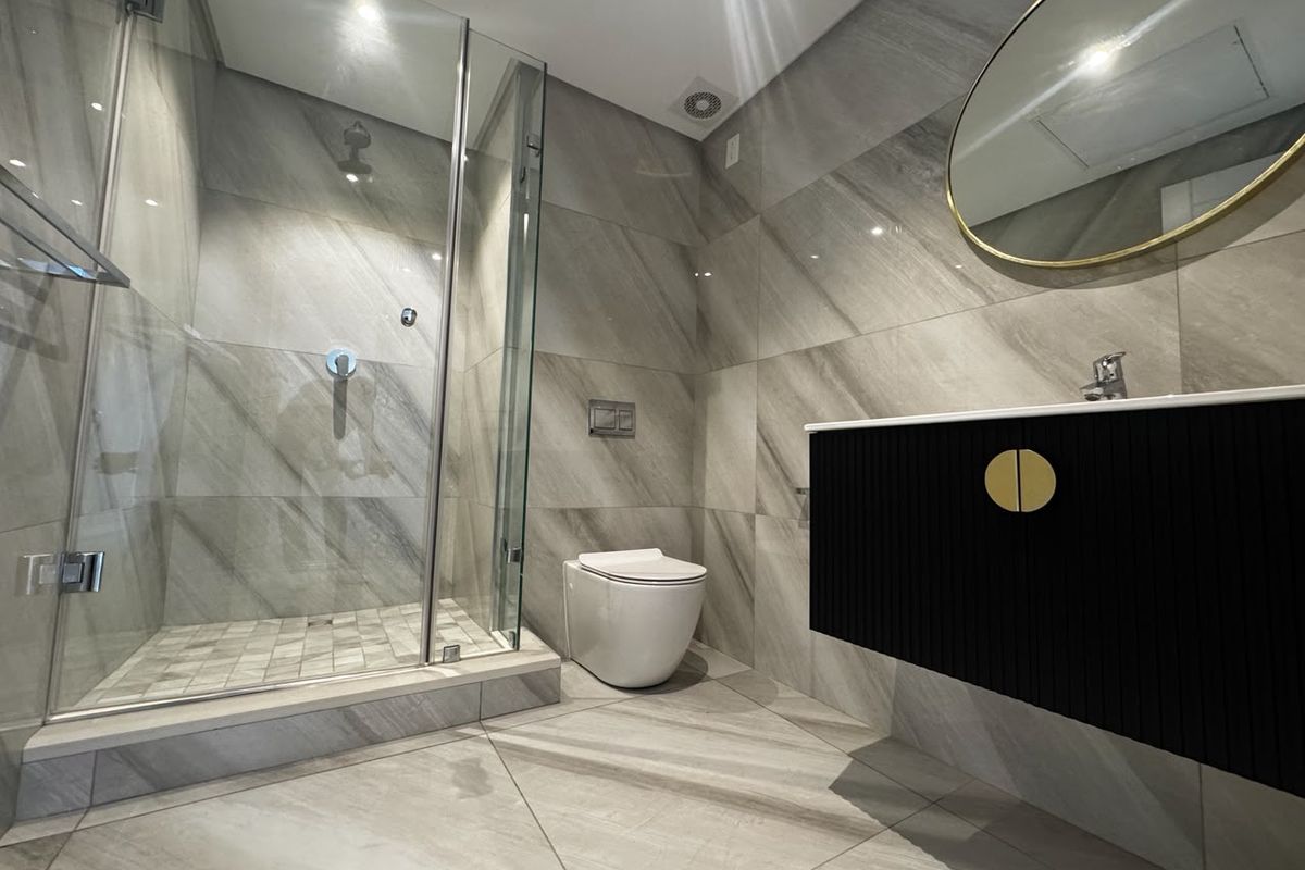 Modern bathroom featuring a glass-enclosed shower, wall-mounted toilet, and a sleek floating vanity with contemporary finishes and large format tiling.