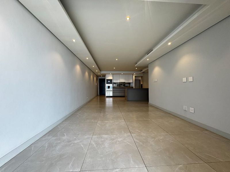 Spacious open-plan living area featuring large-format porcelain floor tiles, recessed ceiling lighting, and a modern kitchen with integrated appliances and a central island.