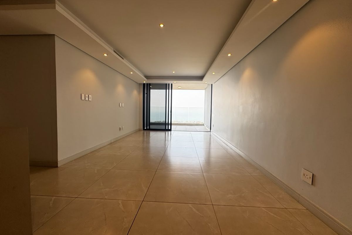A bright, empty living area featuring polished tile flooring, recessed ceiling lighting, and a large sliding glass door leading to an outdoor balcony.