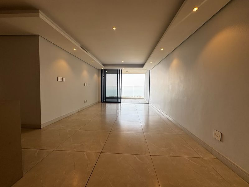 A bright, empty living area featuring polished tile flooring, recessed ceiling lighting, and a large sliding glass door leading to an outdoor balcony.