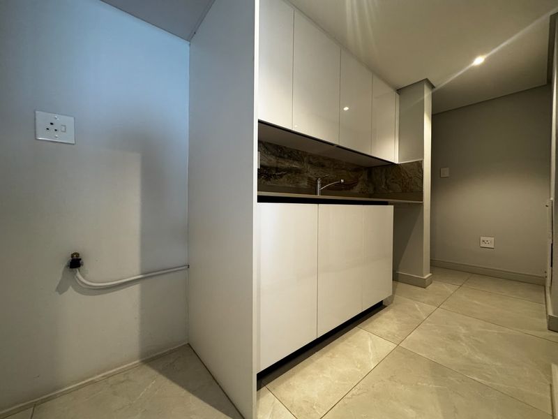A clean, modern laundry area featuring sleek white built-in cabinetry, a sink, and tiled flooring with dedicated plumbing connections.