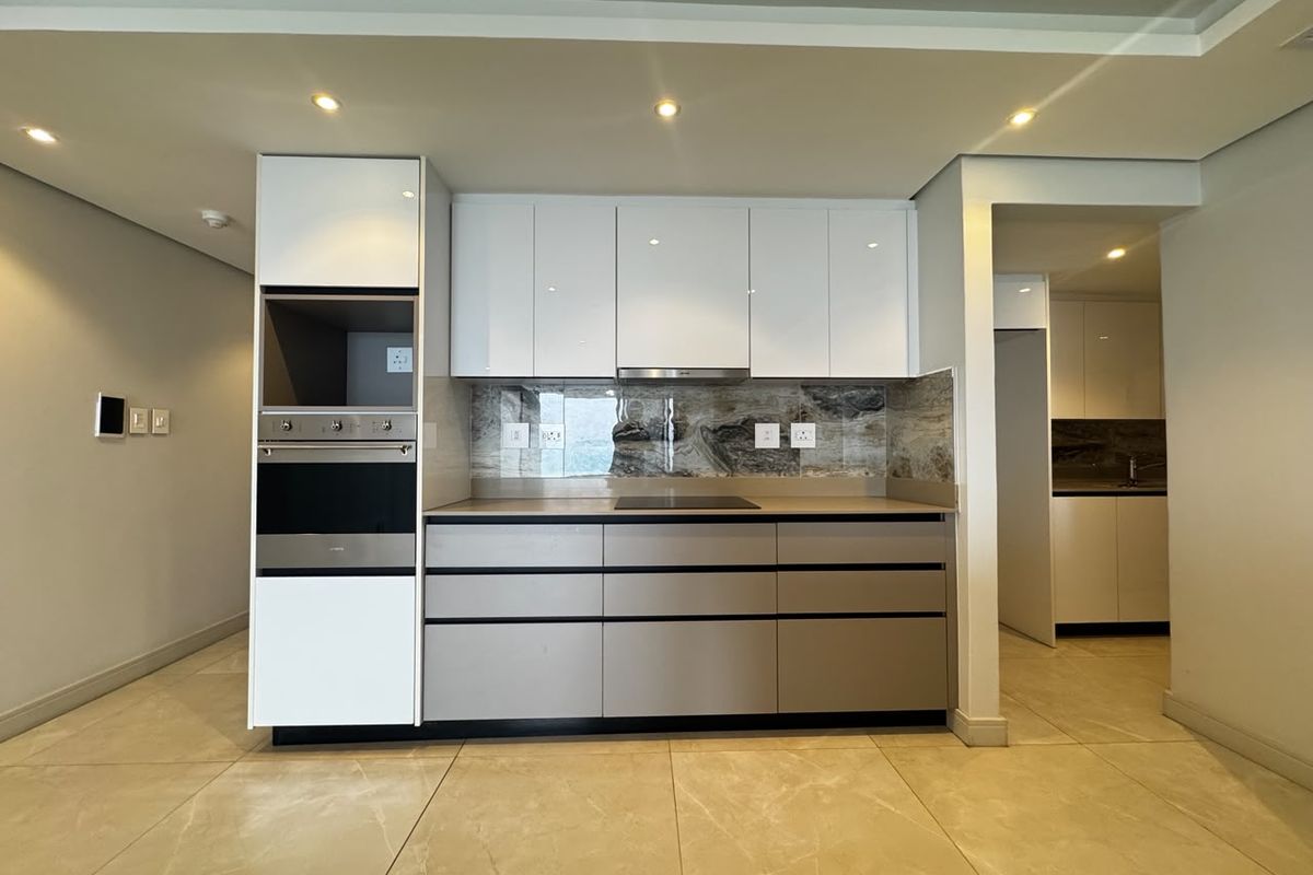 Modern kitchen featuring sleek handleless cabinetry, built-in oven and microwave, induction hob, and elegant stone splashback with recessed lighting.