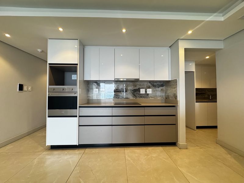 Modern kitchen featuring sleek handleless cabinetry, built-in oven and microwave, induction hob, and elegant stone splashback with recessed lighting.