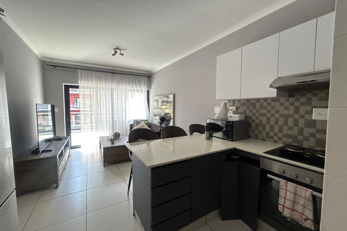 Open-plan living area featuring a modern kitchen with stone countertops, built-in appliances, and tiled flooring, leading to a bright balcony through sliding glass doors.