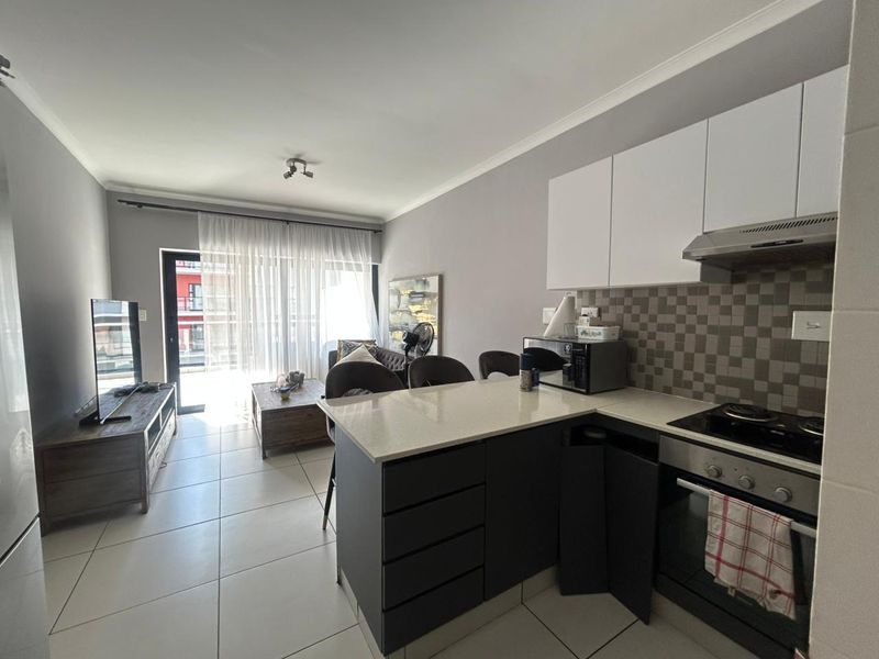 Open-plan living area featuring a modern kitchen with stone countertops, built-in appliances, and tiled flooring, leading to a bright balcony through sliding glass doors.