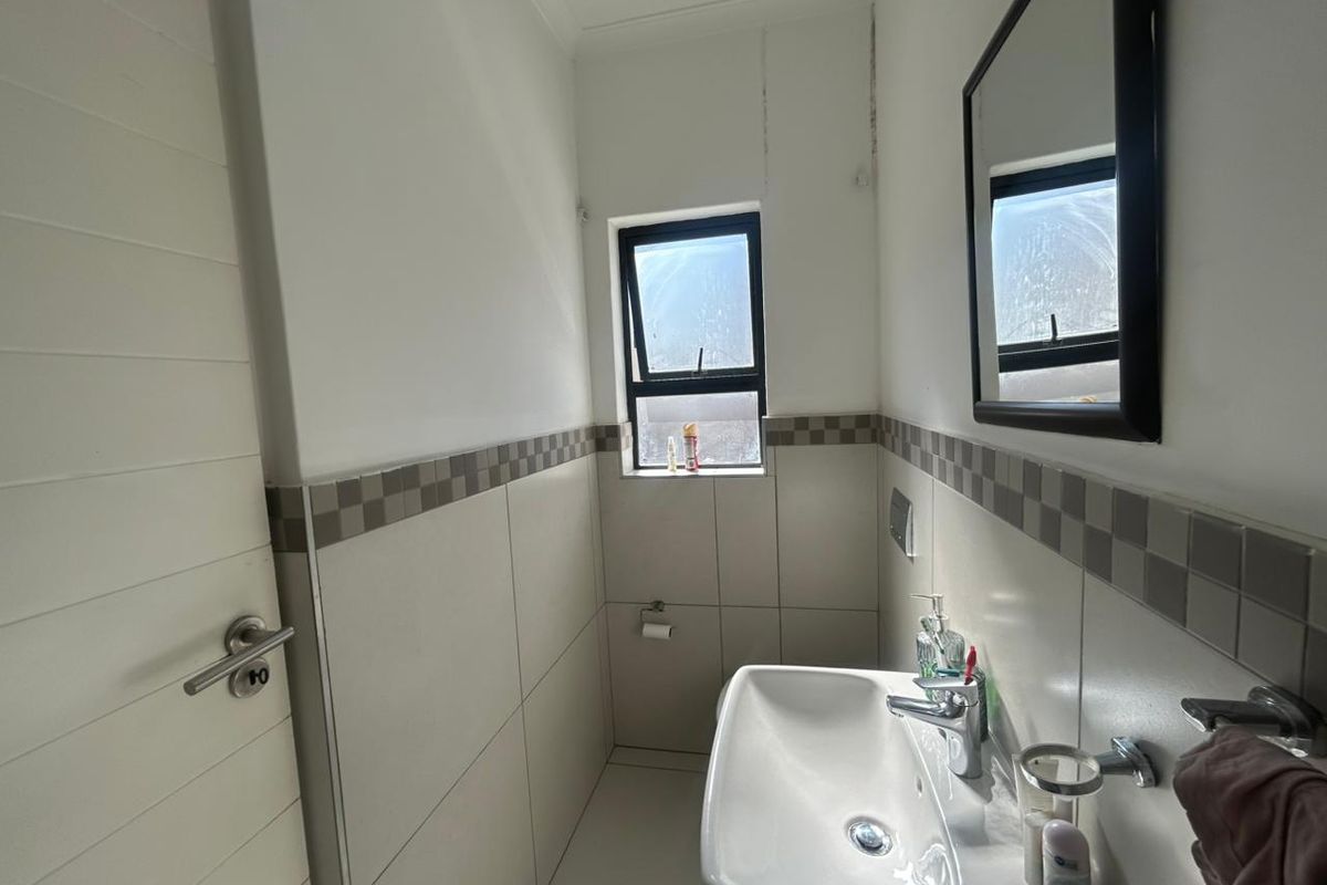 A compact bathroom featuring a wall-mounted basin, chrome fixtures, and neutral wall tiling with a decorative border.