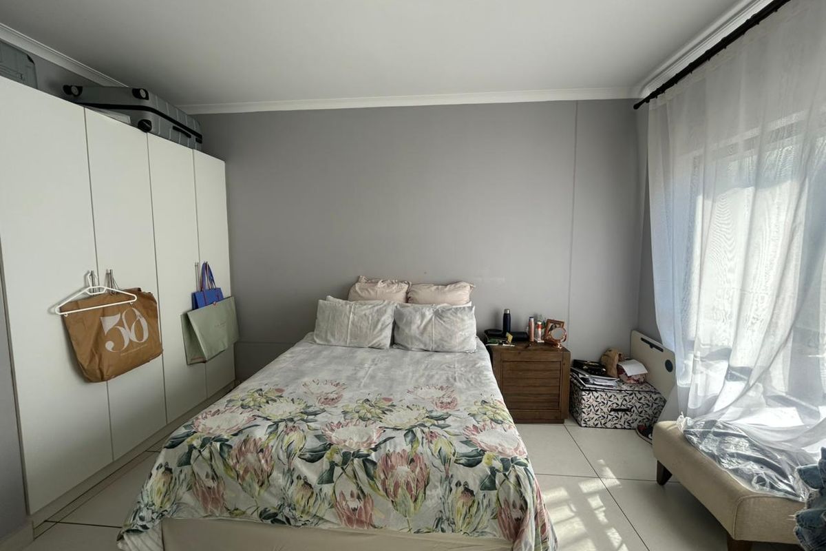 A bedroom featuring built-in cupboards, tiled flooring, and natural light through a window with curtain rails.