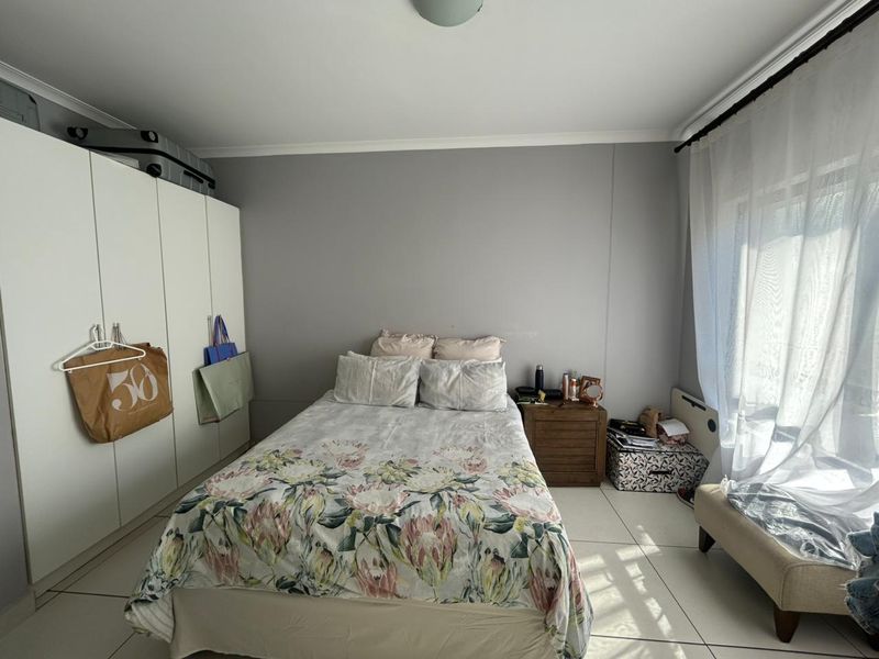 A bedroom featuring built-in cupboards, tiled flooring, and natural light through a window with curtain rails.