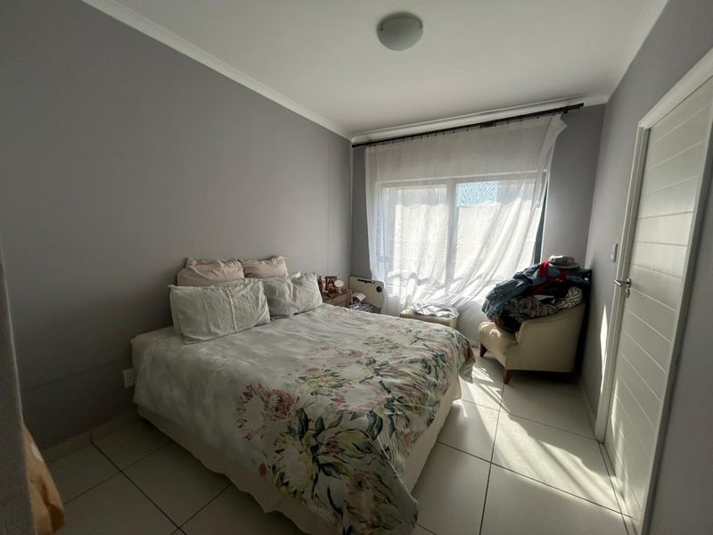 A bedroom featuring neutral grey walls, tiled flooring, and a large window with sheer curtains allowing natural light into the space.
