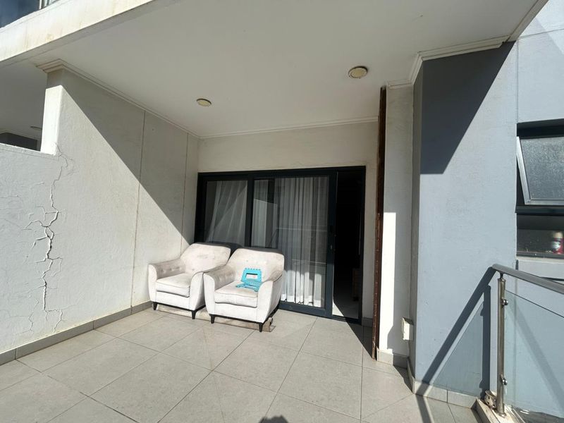 A covered balcony featuring tiled flooring, a glass sliding door entrance, and a glass balustrade, showing some visible cracking on the exterior wall.