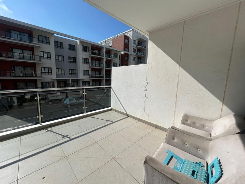 A balcony featuring tiled flooring and a glass balustrade, showing a visible vertical crack on the side wall.