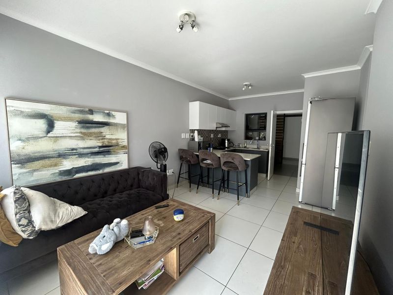 Modern open-plan living area featuring a sleek kitchen with island, neutral tiled flooring, and contemporary grey wall finishes.