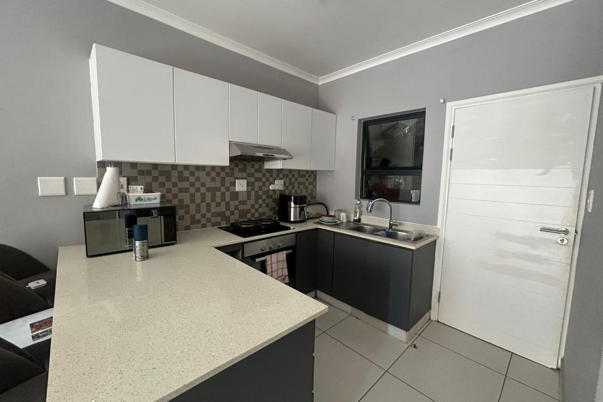 Modern kitchen featuring sleek two-tone cabinetry, quartz countertops, a mosaic tile backsplash, and integrated stainless steel appliances.
