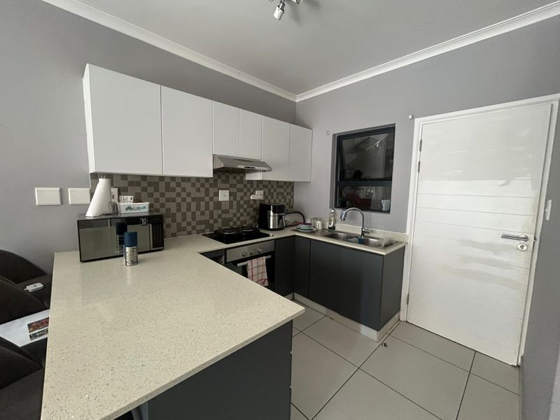 Modern kitchen featuring sleek two-tone cabinetry, quartz countertops, a mosaic tile backsplash, and integrated stainless steel appliances.