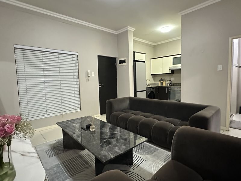 Open-plan living area featuring tiled floors, modern kitchen cabinetry with built-in appliances, and an adjacent bathroom, creating a functional and cohesive apartment layout.