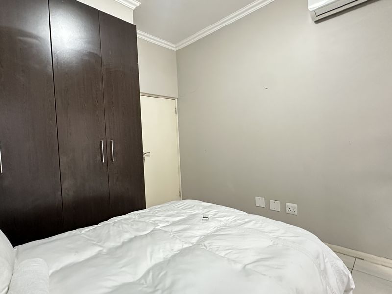 A bedroom featuring dark wood built-in cupboards, crown molding, tiled flooring, and a wall-mounted air conditioning unit.