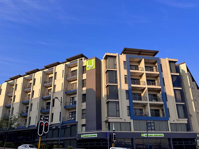 A modern multi-story apartment building featuring a contemporary facade with private balconies, large windows, and prominent commercial signage at street level.